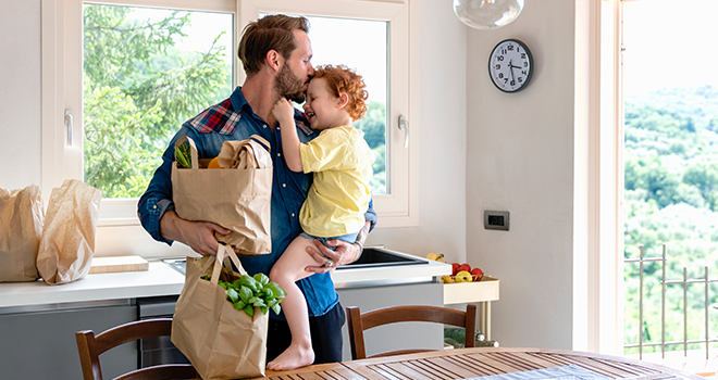 Father holding child and bag of groceries in kitchen